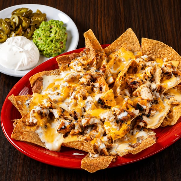 Chicken nachos on a red plate with sides of guacamole, sour cream, and jalapeños.